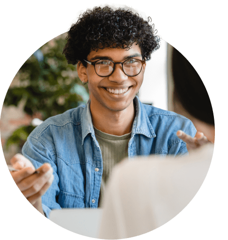 A man in a blue shirt and glasses engages in conversation with a woman during a meeting setting.